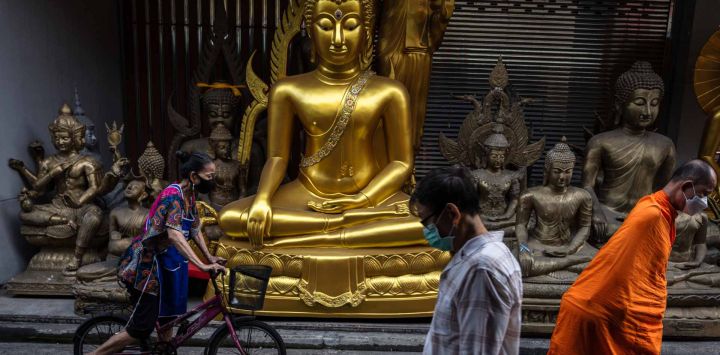 Peatones, incluido un monje, caminan frente a una tienda que vende estatuas de Buda en Bangkok. Foto de chanakarn laosarakham / AFP