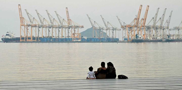 Una familia se sienta frente al telón de fondo de un astillero en la ciudad costera de Fujairah, en el estrecho de Ormuz. Foto de Giuseppe CACACE / AFP