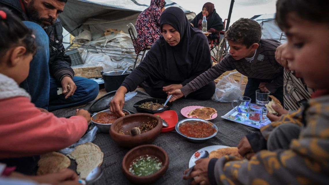 The displaced Palestinian Abu Mustafa family sits together as they break the dawn-to-dusk Ramadan fast during Iftar in the Nuseirat refugee camp in the central Gaza Strip on February 26, 2026.