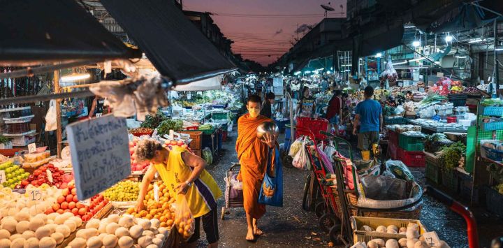 Un monje camina junto a los puestos de vendedores de productos frescos mientras recoge limosnas en el Mercado Khlong Toei en Bangkok. Foto de ANTHONY WALLACE / AFP