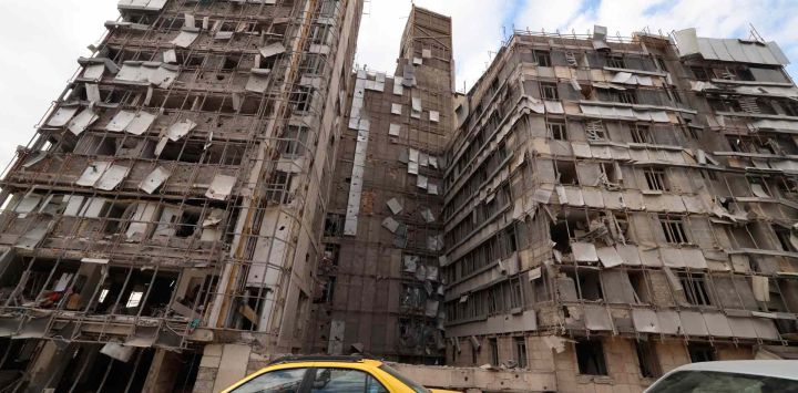 Los automóviles pasan frente a la fachada dañada del Hospital Gandi, Teherán. Foto de ATTA KENARE / AFP