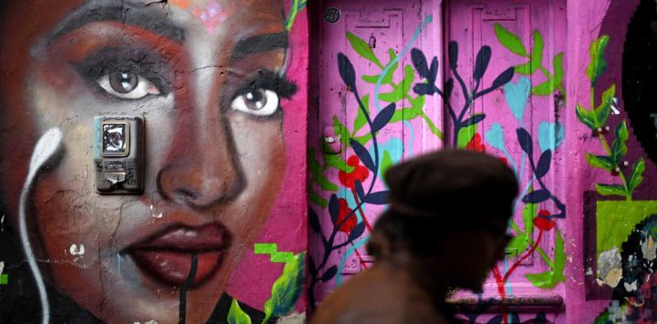 Un hombre camina junto a un grafiti en la pared de una casa en un callejón del barrio La Candelaria en Bogotá. Foto de Pablo VERA / AFP