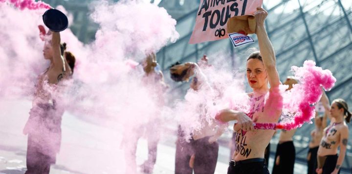 Miembros en topless del grupo activista feminista FEMEN se quitan las máscaras de cerdo y encienden bengalas rosas durante una acción en el Museo del Louvre junto a la Pirámide del Louvre, diseñada por el arquitecto chino-estadounidense Ieoh Ming Pei.
