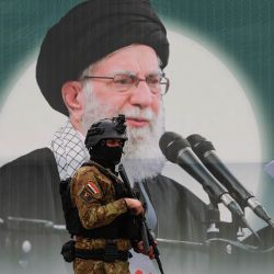 Un miembro de las Fuerzas de Movilización Popular de Irak (Hashed al-Shaabi) se encuentra frente a una pancarta que representa al líder supremo iraní, el ayatolá Ali Jamenei, asesinado en la plaza Tahrir de Bagdad. Según informaron a la AFP dos altos funcionarios de seguridad, ataques aéreos causaron la muerte de al menos nueve combatientes respaldados por Irán en Irak ese mismo día, cerca de la frontera entre Irak y Siria. Irak se vio inmediatamente involucrado en la guerra de Oriente Medio, desencadenada por el ataque de Estados Unidos e Israel contra Irán el 28 de febrero. | Foto:AHMAD AL-RUBAYE / AFP