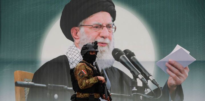 Un miembro de las Fuerzas de Movilización Popular de Irak (Hashed al-Shaabi) se encuentra frente a una pancarta que representa al líder supremo iraní, el ayatolá Ali Jamenei, asesinado en la plaza Tahrir de Bagdad. Según informaron a la AFP dos altos funcionarios de seguridad, ataques aéreos causaron la muerte de al menos nueve combatientes respaldados por Irán en Irak ese mismo día, cerca de la frontera entre Irak y Siria. Irak se vio inmediatamente involucrado en la guerra de Oriente Medio, desencadenada por el ataque de Estados Unidos e Israel contra Irán el 28 de febrero.