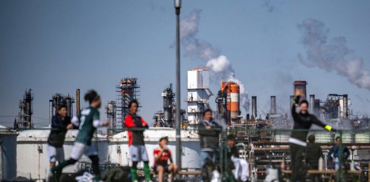 Varias personas juegan al fútbol en el parque Higashi-Ogishima Higashi, mientras se observan tanques de almacenamiento de energía cerca de una refinería de petróleo en la Zona Industrial de Keihin, un importante cinturón industrial de la bahía de Tokio, en la ciudad de Kawasaki, Japón.