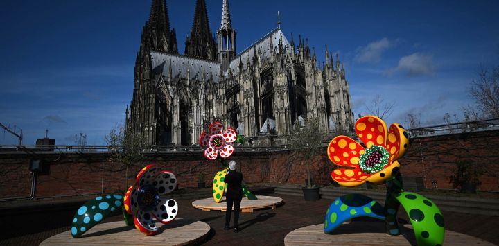 Un visitante toma una foto de la instalación "Flores que hablan de mi corazón entregado al cielo" con la catedral de Colonia de fondo durante la presentación previa de una exposición de la artista japonesa Yayoi Kusama en el Museo Ludwig de Colonia.