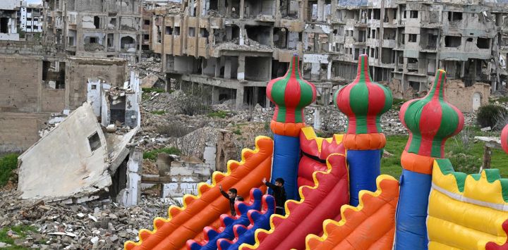 Niños sirios disfrutan de las atracciones de un parque de diversiones instalado en un terreno rodeado de edificios destruidos, el tercer día de Eid al-Fitr, que marca el final del mes sagrado de Ramadán, en el barrio de Jobar, en Damasco. La guerra civil en Siria duró casi 14 años y culminó con la caída del régimen de Assad en diciembre de 2024.