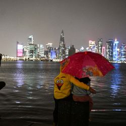 Niños se resguardan bajo un paraguas durante una tormenta en la ciudad de Doha, Qatar. | Foto:Mahmud Hams / AFP