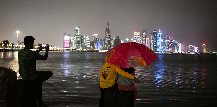 Niños se resguardan bajo un paraguas durante una tormenta en la ciudad de Doha, Qatar.