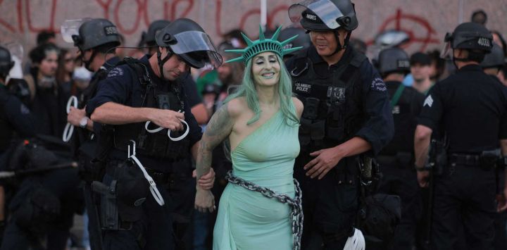 Agentes del Departamento de Policía de Los Ángeles (LAPD) arrestaron a una manifestante vestida como la Estatua de la Libertad encadenada tras enfrentamientos cerca del Centro de Detención Metropolitano durante la jornada nacional de protesta "No Kings" en Los Ángeles. Multitudes de manifestantes se congregaron en todo Estados Unidos contra el presidente Donald Trump, expresando su furia por lo que consideran su estilo de gobierno autoritario, sus políticas migratorias de línea dura y la guerra con Irán. Los organizadores afirmaron que "al menos 8 millones de personas se reunieron en más de 3300 eventos en los 50 estados", tanto en grandes ciudades como en pequeños pueblos. Las autoridades estadounidenses no proporcionaron una estimación nacional de la multitud.