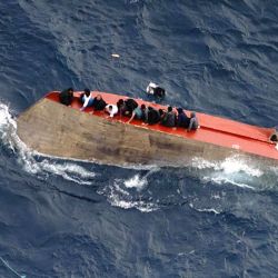 Esta foto tomda y distribuida por la ONG alemana Sea-Watch, muestra a migrantes sentados en una embarcación volcada frente a las costas de Libia. Decenas de personas están desaparecidas tras el naufragio de una embarcación de migrantes en el Mediterráneo central, según informaron las ONG Mediterranea Saving Humans y Sea-Watch en redes sociales. Dos personas fallecieron y 32 fueron rescatadas de la embarcación, que había zarpado de Libia con aproximadamente 105 personas a bordo, según Mediterranea Saving Humans. | Foto:FABIAN MELBER / SEA-WATCH / AFP