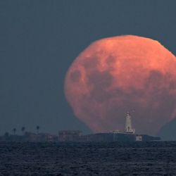 La luna en fase gibosa menguante se eleva tras la isla de Flores y su faro, frente a la costa de Montevideo, Uruguay. | Foto:MARIANA SUAREZ / AFP