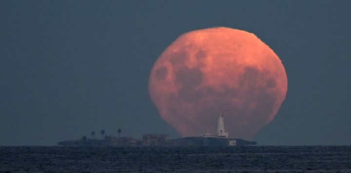 La luna en fase gibosa menguante se eleva tras la isla de Flores y su faro, frente a la costa de Montevideo, Uruguay.