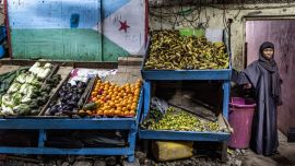 Una mujer se encuentra junto a un puesto decorado con la bandera de Yibuti en un mercado al aire libre, mientras los residentes salen a las calles durante las horas más frescas de la tarde para escapar del calor del día en el centro de Yibuti, antes de las elecciones presidenciales de Yibuti de 2026.