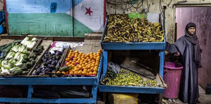 Una mujer se encuentra junto a un puesto decorado con la bandera de Yibuti en un mercado al aire libre, mientras los residentes salen a las calles durante las horas más frescas de la tarde para escapar del calor del día en el centro de Yibuti, antes de las elecciones presidenciales de Yibuti de 2026.
