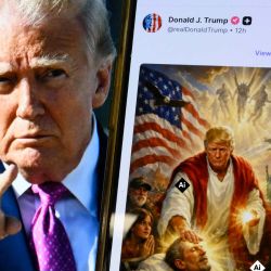 Una imagen del presidente estadounidense Donald Trump en una pantalla y una imagen generada por IA que publicó en su plataforma Truth Social, donde se representa a sí mismo como Jesucristo tras criticar al papa León XIV. Posteriormente, Trump publicó una imagen generada por IA que aparentemente lo representa como Jesucristo. En la imagen, el presidente aparece vestido con túnicas rojas y blancas curando a un hombre con su mano sanadora. La bandera estadounidense se muestra sobre su hombro. Trump y la Casa Blanca ya habían compartido imágenes generadas por IA, incluyendo una en la que el presidente aparecía vestido como el papa. | Foto:Mandel Ngan / AFP