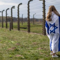Una mujer envuelta en la bandera de Israel observa la alambrada del antiguo campo de exterminio nazi de Auschwitz-Birkenau en Brzezinka (Birkenau), cerca de Oswiecim, Polonia, durante la Marcha de la Vida anual en honor a las víctimas del Holocausto. | Foto:WOJTEK RADWANSKI / AFP