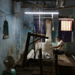 Un niño observa a un artesano mientras teje un sari Banarasi en un telar manual en un taller en Varanasi, India. | Foto:NIHARIKA KULKARNI / AFP