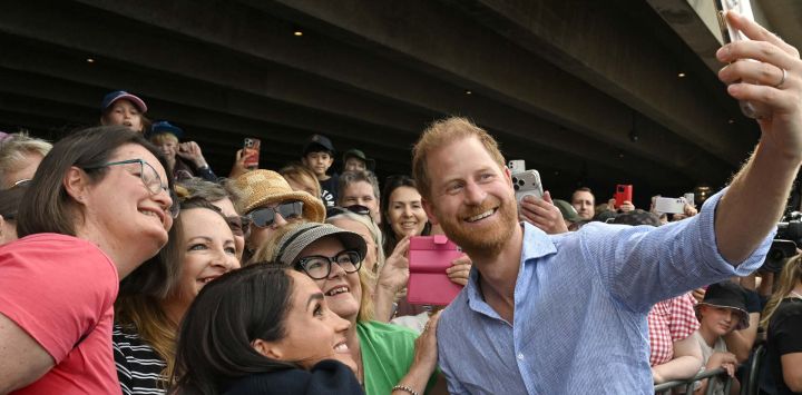 El príncipe Harry de Gran Bretaña, duque de Sussex, y su esposa Meghan, duquesa de Sussex, posan para selfies con miembros del público bajo las escalinatas de la emblemática Ópera de Sídney, Australia.