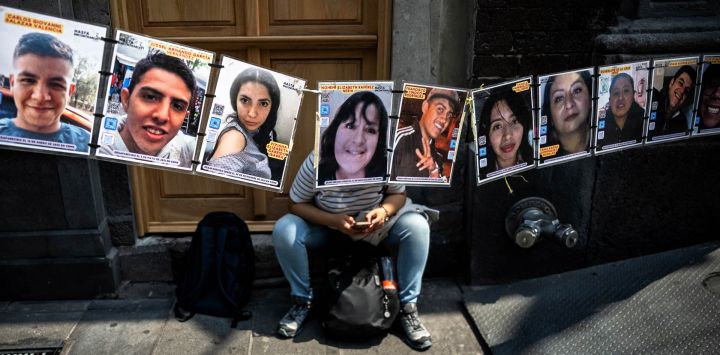 Una mujer se sienta detrás de fotografías de personas desaparecidas mientras manifestantes y familiares protestan frente al Centro Cultural Español en Ciudad de México, mientras el Alto Comisionado de las Naciones Unidas para los Derechos Humanos, Volker Turk, celebra una reunión dentro del edificio.