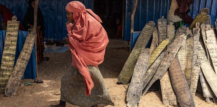 Una niña desplazada interna asiste a una clase en una madrasa para leer versículos coránicos grabados en trozos de madera en un campamento para desplazados en las afueras de la ciudad de Kismayo. Millones de personas en Somalia sufren las repercusiones de una grave sequía tras tres temporadas de lluvias consecutivas sin precipitaciones. Kismayo, capital del estado de Jubaland, en el sur de Somalia, es una de las ciudades que más desplazados internos recibe en este país del Cuerno de África, acogiendo a cientos de miles de personas que huyen de la prolongada sequía y el conflicto. Save the Children proporciona servicios de salud y nutrición en todo el campamento.