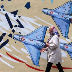 Esta foto muestra a una mujer caminando junto a un mural antiestadounidense y antiisraelí en Teherán. Desde el estallido de la guerra entre Irán, Israel y Estados Unidos, han surgido coloridos murales en Teherán y sus alrededores, ricos en simbolismo y con temas de resistencia y desafío. Los murales y las pancartas han sido durante mucho tiempo un rasgo distintivo del paisaje urbano iraní, particularmente en Teherán, donde estas pinturas en las plazas centrales a menudo reflejan el mensaje político y la postura de política exterior del Estado. | Foto:ATTA KENARE / AFP