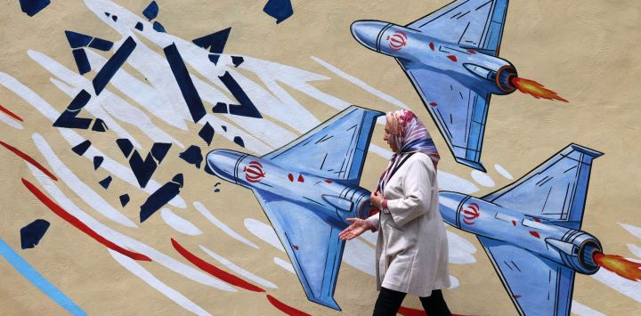 Esta foto muestra a una mujer caminando junto a un mural antiestadounidense y antiisraelí en Teherán. Desde el estallido de la guerra entre Irán, Israel y Estados Unidos, han surgido coloridos murales en Teherán y sus alrededores, ricos en simbolismo y con temas de resistencia y desafío. Los murales y las pancartas han sido durante mucho tiempo un rasgo distintivo del paisaje urbano iraní, particularmente en Teherán, donde estas pinturas en las plazas centrales a menudo reflejan el mensaje político y la postura de política exterior del Estado.