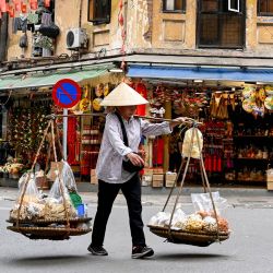 Un vendedor ambulante camina por una calle llevando comida para vender en Hanói, Vietnam. | Foto:NHAC NGUYEN / AFP