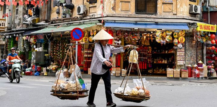 Un vendedor ambulante camina por una calle llevando comida para vender en Hanói, Vietnam.