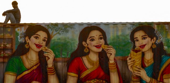 Un hombre descansa sobre contenedores metálicos decorados con obras de arte a las afueras de un recinto ferial en Bombay, India.