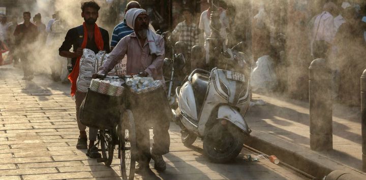 Varias personas caminan bajo los aspersores de agua instalados a lo largo de una calle en un caluroso día de verano en Varanasi, India.