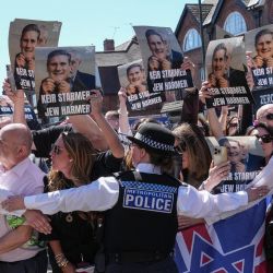 La policía contiene a manifestantes con pancartas mientras un coche (no aparece en la imagen) que transporta al primer ministro británico, Keir Starmer, pasa durante su visita a un centro de ambulancias que presta servicio a la comunidad judía en el barrio de Golders Green, al norte de Londres, un día después de que dos hombres fueran apuñalados en un ataque. El gobierno británico anunció fondos adicionales para patrullas de seguridad en las inmediaciones de sinagogas y escuelas, mientras los líderes comunitarios lo acusaban de no protegerlos, un día después del último ataque contra la comunidad judía. | Foto:CARLOS JASSO / AFP