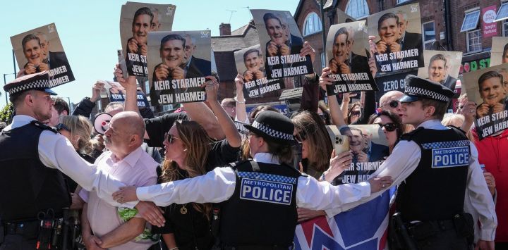 La policía contiene a manifestantes con pancartas mientras un coche (no aparece en la imagen) que transporta al primer ministro británico, Keir Starmer, pasa durante su visita a un centro de ambulancias que presta servicio a la comunidad judía en el barrio de Golders Green, al norte de Londres, un día después de que dos hombres fueran apuñalados en un ataque. El gobierno británico anunció fondos adicionales para patrullas de seguridad en las inmediaciones de sinagogas y escuelas, mientras los líderes comunitarios lo acusaban de no protegerlos, un día después del último ataque contra la comunidad judía.