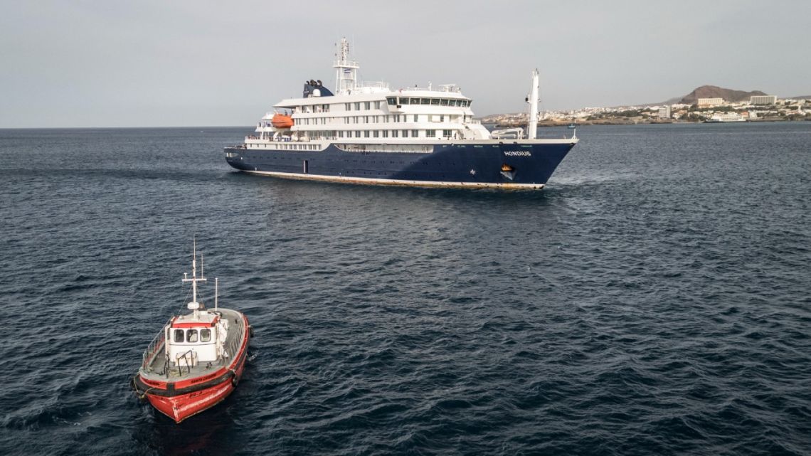 This aerial view shows a boat heading towards the port from the cruise ship MV Hondius, stationary off the port of Praia, the capital of Cape Verde, on May 6, 2026. Evacuations were taking place on May 6, 2026 from a cruise ship stricken with a deadly…