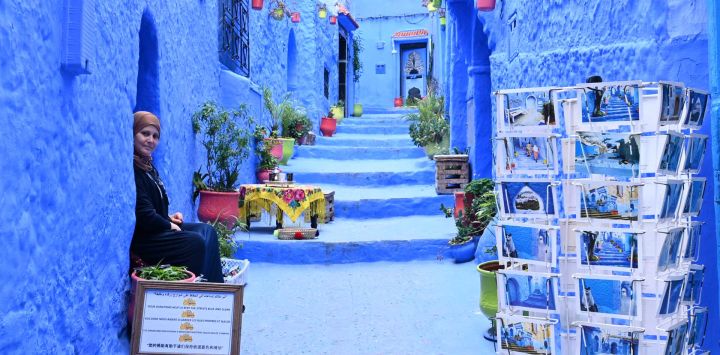 Imagen de una mujer sentada en un callejón, en Chefchaouen, Marruecos. Chefchaouen, conocida como la "ciudad azul" por sus paredes y callejones de colores, es un destino turístico en el norte de Marruecos.