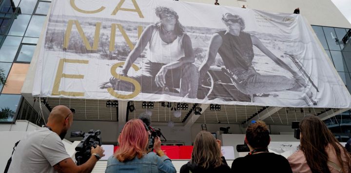 Trabajadores cuelgan el cartel oficial de la 79ª edición del Festival de Cine de Cannes en la fachada del Palais des Festivals mientras periodistas usan cámaras para capturar imágenes en Cannes, sureste de Francia.