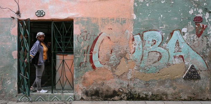 Una mujer se asoma por la puerta de su casa, junto a un muro con un grafiti que dice "CUBA", en una calle de La Habana, Cuba. La Habana acusó a Marco Rubio de "mentir" después de que el Secretario de Estado de Estados Unidos declarara que Washington no había impuesto un embargo petrolero a Cuba y atribuyera la actual crisis energética de la isla a una mala gestión interna.