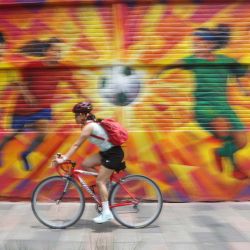 Imagen de una mujer conduciendo una bicicleta frente a un grafiti con la temática de fútbol, en la ciudad de México, capital de México. México  será coanfitrión de la Copa Mundial Fifa 2026 en junio y julio de este año, junto con Estados Unidos y Canadá, convirtiéndose en el primer país del mundo en albergar tres torneos de la Copa Mundial. | Foto:Xinhua/Francisco Cañedo