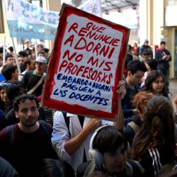 Un manifestante sostiene un cartel que dice : "Adorni debería renunciar, no mis maestros", durante una protesta convocada por estudiantes y trabajadores universitarios contra las políticas del gobierno de Javier Milei en la estación de tren de Retiro en Buenos Aires. | Foto:LUIS ROBAYO / AFP