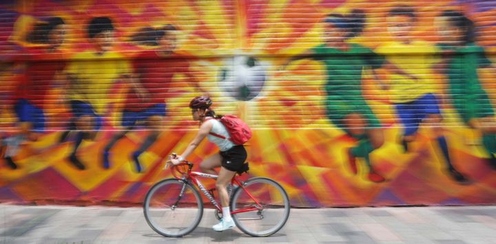 Imagen de una mujer conduciendo una bicicleta frente a un grafiti con la temática de fútbol, en la ciudad de México, capital de México. México  será coanfitrión de la Copa Mundial Fifa 2026 en junio y julio de este año, junto con Estados Unidos y Canadá, convirtiéndose en el primer país del mundo en albergar tres torneos de la Copa Mundial.