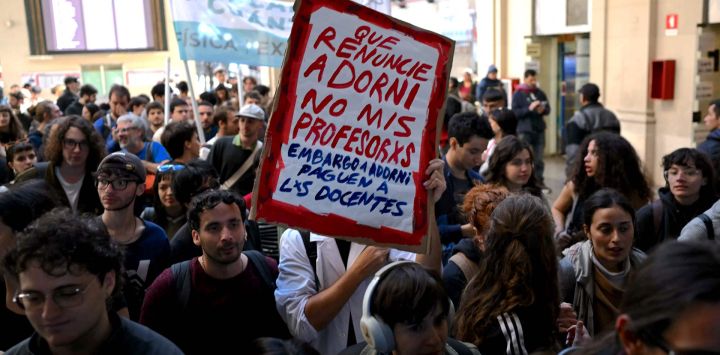 Un manifestante sostiene un cartel que dice : "Adorni debería renunciar, no mis maestros", durante una protesta convocada por estudiantes y trabajadores universitarios contra las políticas del gobierno de Javier Milei en la estación de tren de Retiro en Buenos Aires.