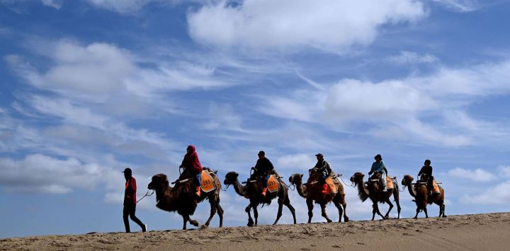 Turistas montan camellos en el Area Escénica de la Montaña Mingsha y el Manantial de la Luna Creciente después de la lluvia, en la ciudad de Dunhuang, en la provincia de Gansu, en el noroeste de China.