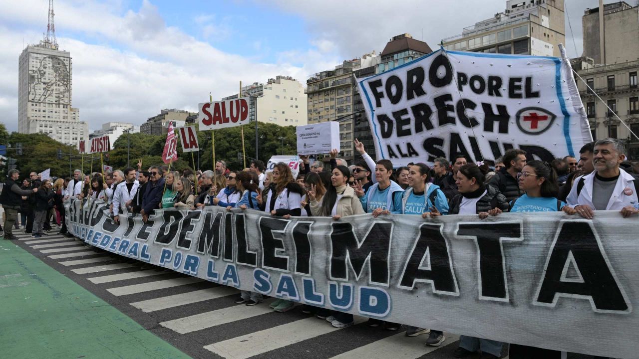 Trabajadores portan una pancarta con el lema "Las medidas de austeridad de Milei son mortales" mientras marchan desde el edificio del Ministerio de Salud (izquierda), cuya fachada luce una imagen de Eva Perón, hasta la Plaza de Mayo durante una protesta en defensa de la salud pública contra los recortes gubernamentales en Buenos Aires. | Foto:JUAN MABROMATA / AFP