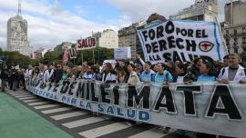 Trabajadores portan una pancarta con el lema "Las medidas de austeridad de Milei son mortales" mientras marchan desde el edificio del Ministerio de Salud (izquierda), cuya fachada luce una imagen de Eva Perón, hasta la Plaza de Mayo durante una protesta en defensa de la salud pública contra los recortes gubernamentales en Buenos Aires.