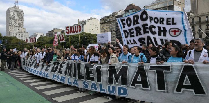 Trabajadores portan una pancarta con el lema "Las medidas de austeridad de Milei son mortales" mientras marchan desde el edificio del Ministerio de Salud (izquierda), cuya fachada luce una imagen de Eva Perón, hasta la Plaza de Mayo durante una protesta en defensa de la salud pública contra los recortes gubernamentales en Buenos Aires.