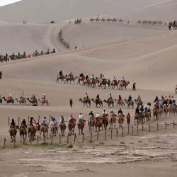 Turistas montan camellos en el Area Escénica de la Montaña Mingsha y el Manantial de la Luna Creciente, en Dunhuang, en la provincia de Gansu, en el noroeste de China. | Foto:Xinhua/Zhang Xiaoliang
