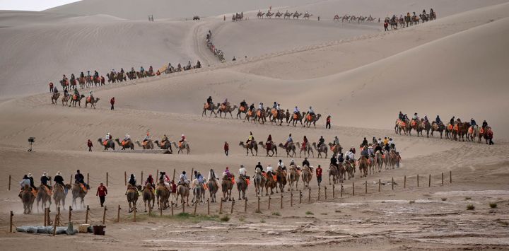 Turistas montan camellos en el Area Escénica de la Montaña Mingsha y el Manantial de la Luna Creciente, en Dunhuang, en la provincia de Gansu, en el noroeste de China.