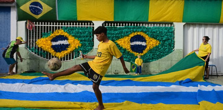 Un niño controla la pelota frente a una casa decorada con motivos de la bandera nacional brasileña en preparación para la Copa Mundial de la FIFA 2026, en Brasilia, Brasil.