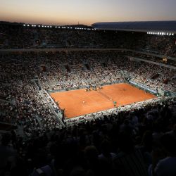 El sol se pone sobre la pista Philippe-Chatrier mientras el francés Gael Monfils (derecha) se enfrenta al también francés Hugo Gaston (izquierda) en su partido individual masculino del segundo día del torneo de tenis Roland-Garros en París. | Foto:ALAIN JOCARD / AFP